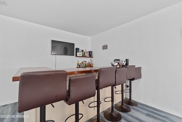 bar featuring a bar, wood finished floors, and baseboards