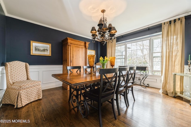 dining area featuring crown molding, a chandelier, a wainscoted wall, wood finished floors, and a decorative wall