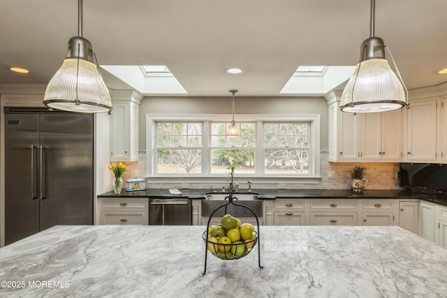 kitchen featuring dark stone countertops, decorative backsplash, appliances with stainless steel finishes, and a skylight