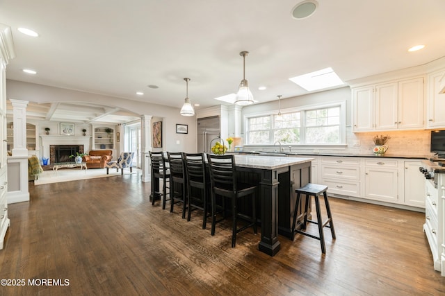 kitchen with a kitchen breakfast bar, a kitchen island, dark wood-style floors, white cabinetry, and ornate columns