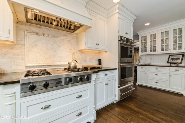 kitchen with glass insert cabinets, dark wood-type flooring, appliances with stainless steel finishes, exhaust hood, and white cabinetry