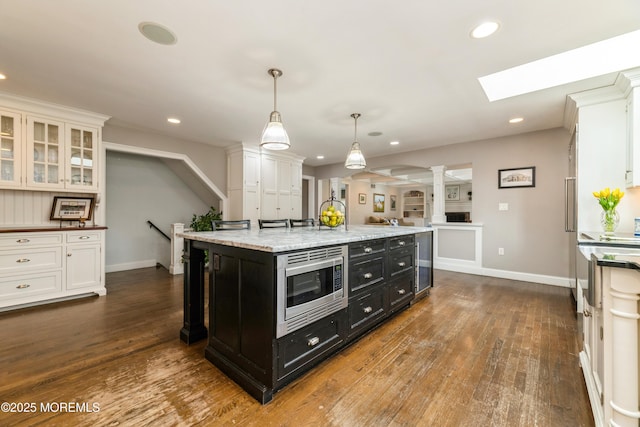 kitchen featuring stainless steel microwave, dark cabinetry, dark wood finished floors, white cabinetry, and decorative columns