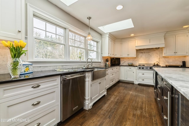 kitchen featuring a skylight, stainless steel appliances, decorative backsplash, dark wood-type flooring, and white cabinetry