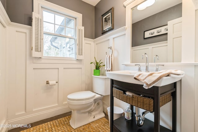 half bath with a decorative wall, toilet, and a wainscoted wall