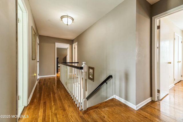 corridor featuring baseboards, an upstairs landing, and wood finished floors