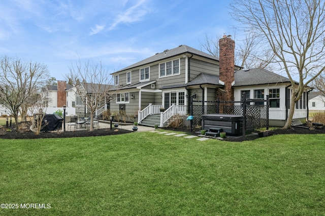 rear view of property with a patio area, a chimney, a hot tub, and a yard