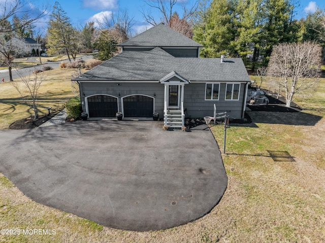 view of front of house with aphalt driveway, an attached garage, a front lawn, and roof with shingles