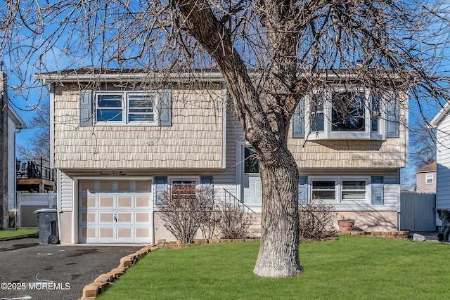 raised ranch featuring aphalt driveway, an attached garage, a front lawn, and fence