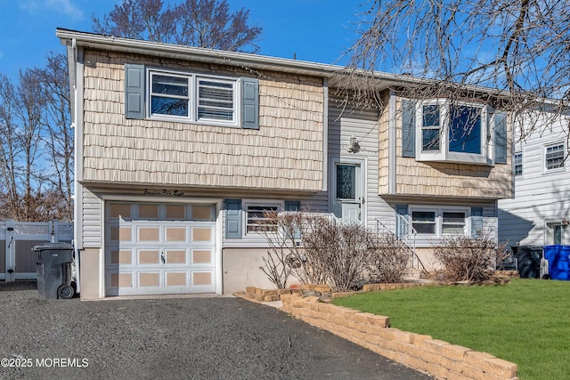 raised ranch with a front lawn, fence, driveway, and an attached garage