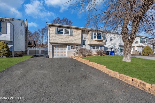 bi-level home with a garage, a front lawn, fence, and aphalt driveway