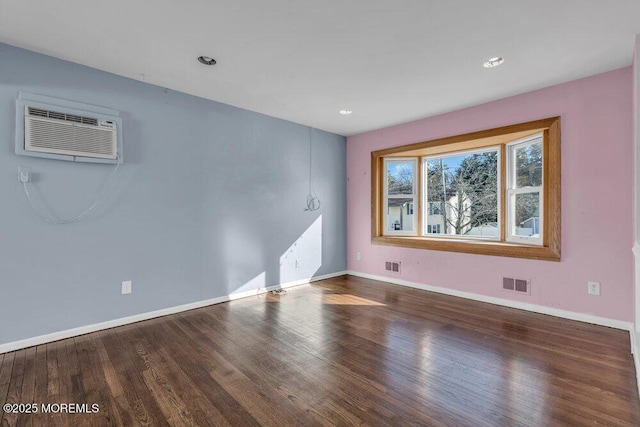 empty room with a wall unit AC, wood finished floors, visible vents, and baseboards