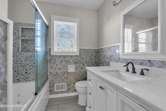 full bath with visible vents, toilet, combined bath / shower with glass door, vanity, and tile walls