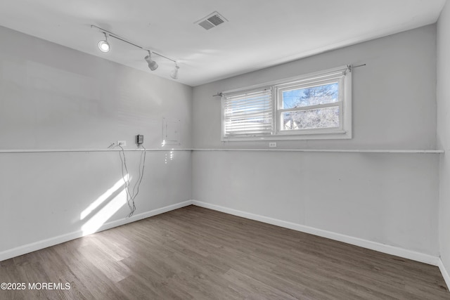 spare room featuring track lighting, wood finished floors, visible vents, and baseboards