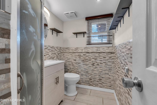 full bathroom with tile walls, visible vents, toilet, vanity, and tile patterned floors