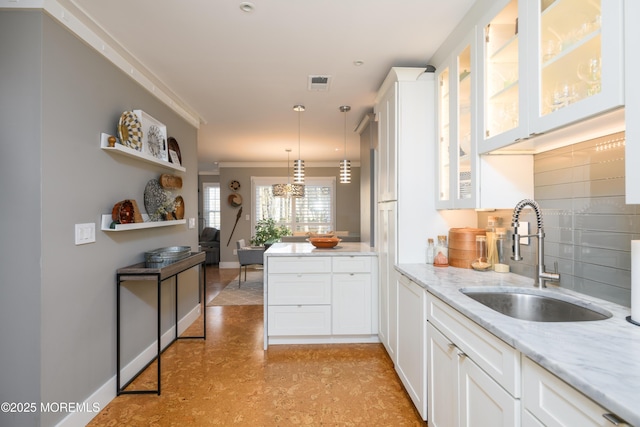 kitchen with glass insert cabinets, light stone countertops, pendant lighting, white cabinetry, and a sink