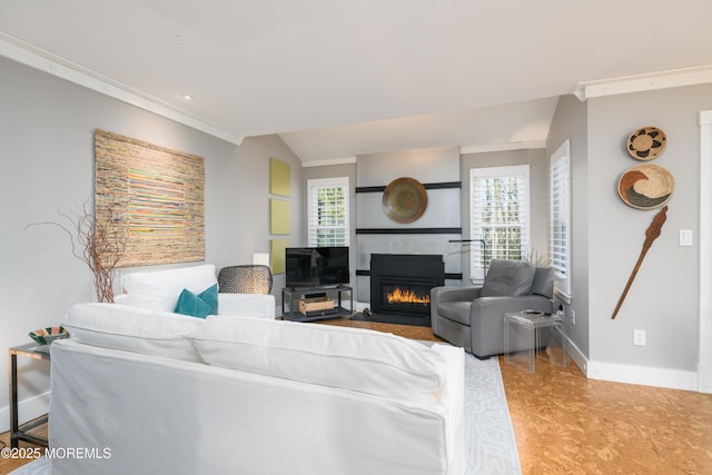 living room featuring baseboards, vaulted ceiling, ornamental molding, recessed lighting, and a glass covered fireplace