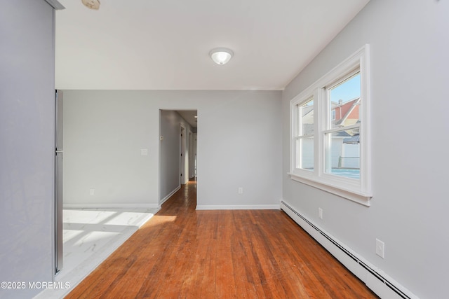 empty room featuring a baseboard radiator, baseboards, and wood finished floors