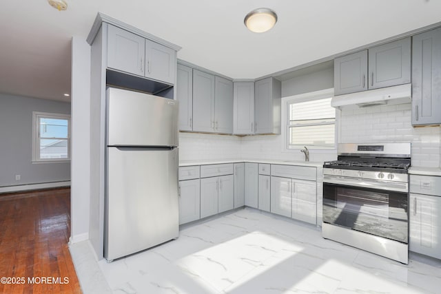 kitchen featuring appliances with stainless steel finishes, gray cabinets, a baseboard heating unit, and under cabinet range hood