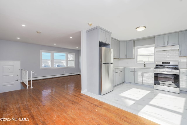 kitchen featuring tasteful backsplash, gray cabinets, stainless steel appliances, under cabinet range hood, and a baseboard heating unit