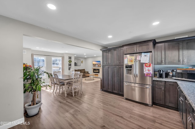 kitchen with light wood finished floors, appliances with stainless steel finishes, dark brown cabinetry, and light stone countertops