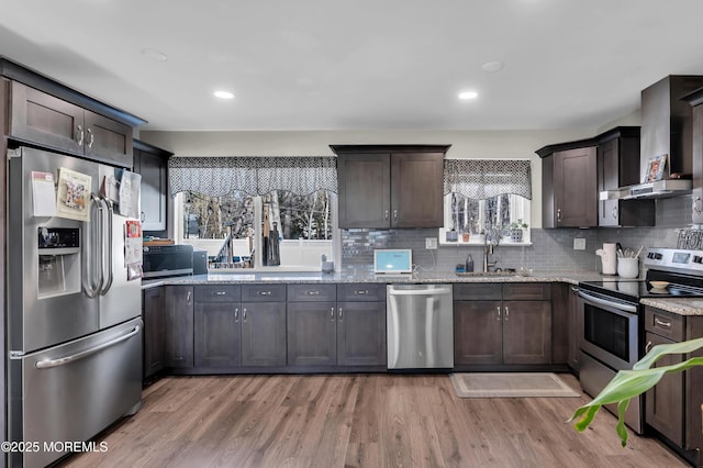 kitchen featuring stainless steel appliances, wall chimney range hood, a sink, and dark brown cabinetry