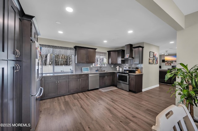 kitchen featuring wall chimney exhaust hood, appliances with stainless steel finishes, wood finished floors, dark brown cabinets, and a sink