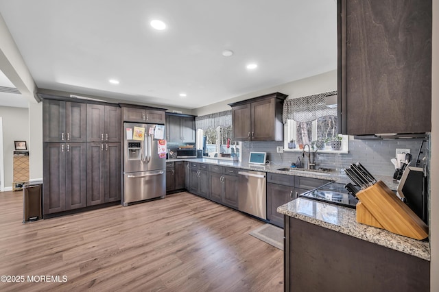 kitchen featuring light stone counters, stainless steel appliances, light wood-style flooring, a sink, and dark brown cabinets