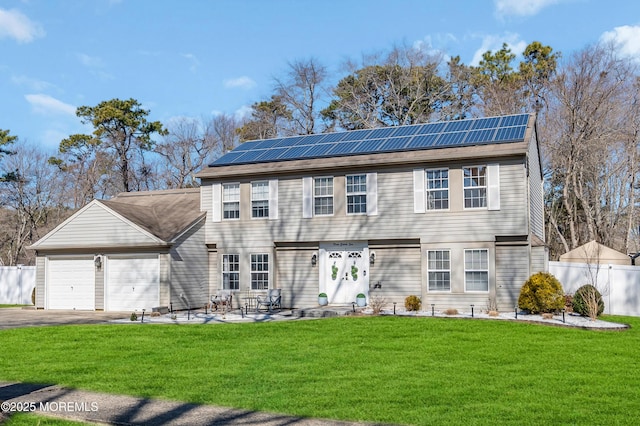 colonial home featuring an attached garage, roof mounted solar panels, fence, and a front lawn