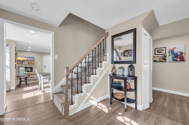 stairs featuring baseboards, wood finished floors, and a glass covered fireplace