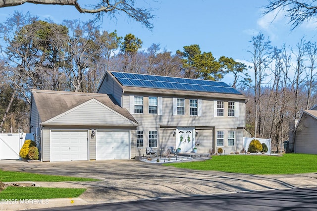 colonial-style house featuring aphalt driveway, solar panels, fence, a garage, and a front lawn