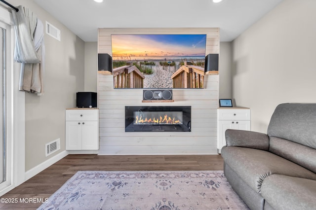 living room featuring a glass covered fireplace, dark wood-style flooring, visible vents, and baseboards