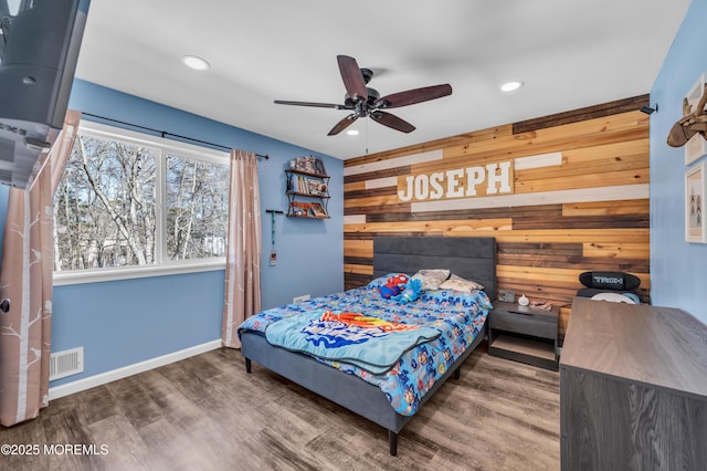 bedroom featuring an accent wall, visible vents, wood walls, and wood finished floors