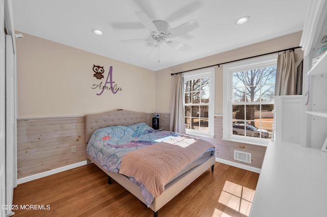 bedroom with a wainscoted wall, wood finished floors, visible vents, and wooden walls