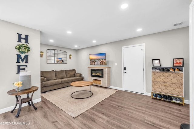 living area featuring a glass covered fireplace, visible vents, recessed lighting, and wood finished floors