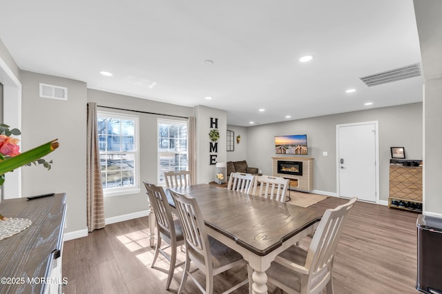 dining space featuring a glass covered fireplace, visible vents, recessed lighting, and wood finished floors