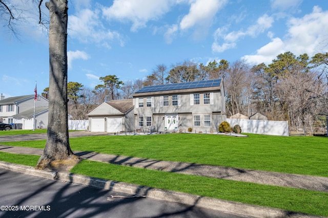 colonial-style house featuring aphalt driveway, a garage, fence, roof mounted solar panels, and a front yard