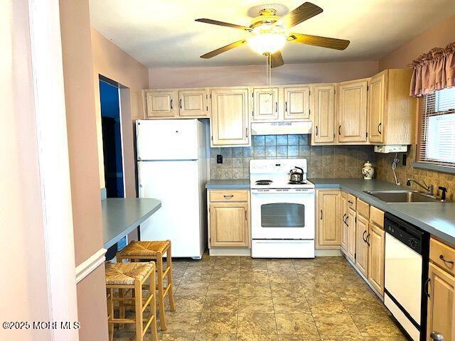 kitchen with white appliances, a sink, under cabinet range hood, and decorative backsplash