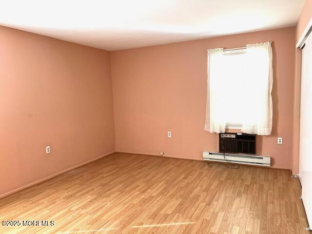 unfurnished room with light wood-style floors and a baseboard radiator