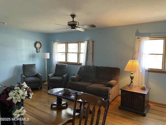 living room with a ceiling fan, baseboards, visible vents, and light wood finished floors