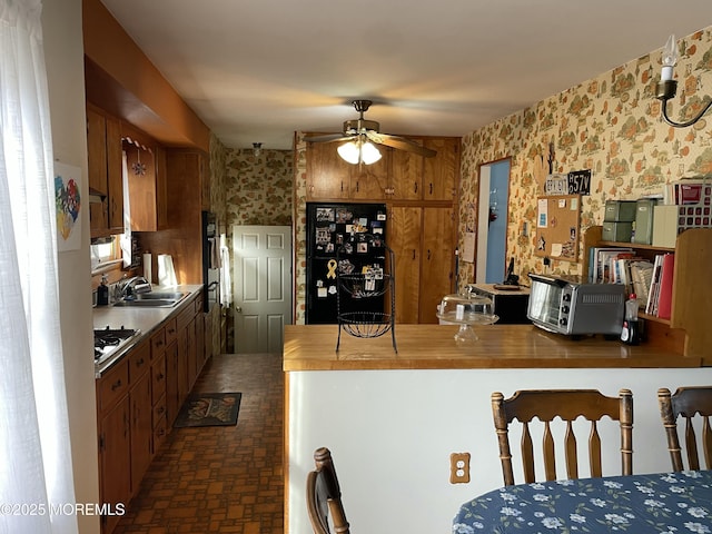 kitchen featuring ceiling fan, stainless steel gas cooktop, a sink, freestanding refrigerator, and wallpapered walls