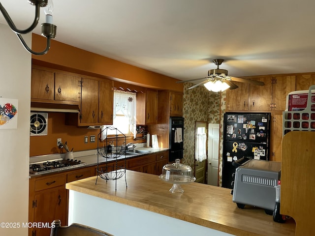 kitchen with a sink, wood counters, a ceiling fan, brown cabinets, and black appliances