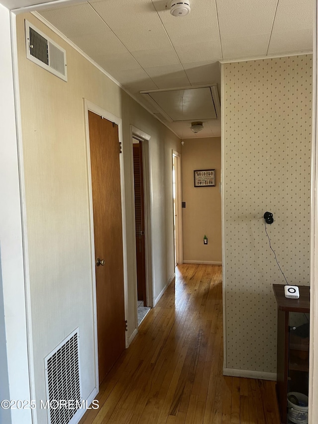 hallway with wood-type flooring, visible vents, and baseboards