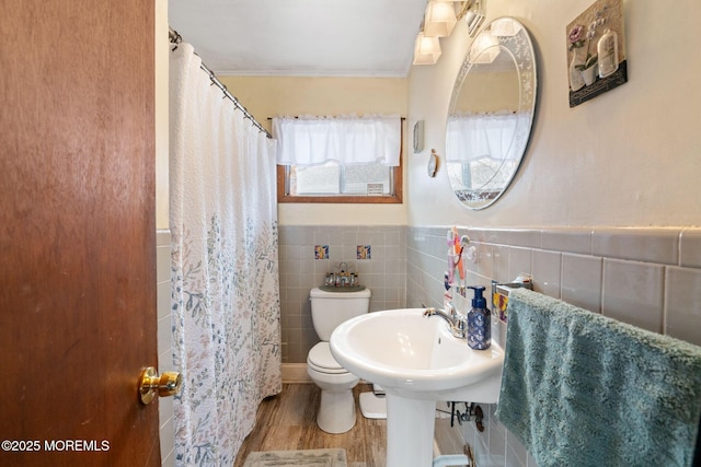 full bath featuring toilet, wood finished floors, tile walls, ornamental molding, and wainscoting