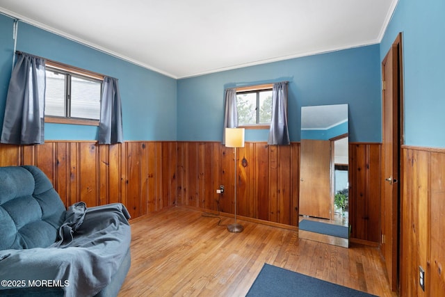 sitting room with ornamental molding, a wainscoted wall, wood walls, and wood finished floors