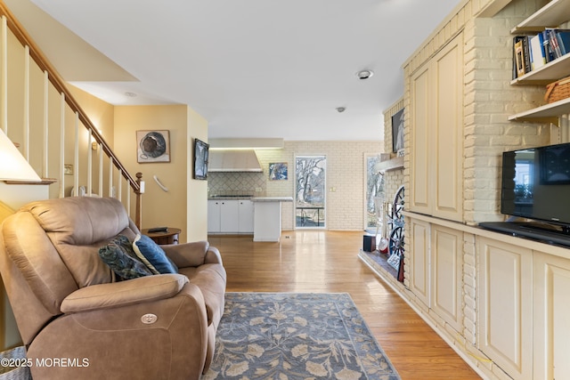 living area featuring brick wall, light wood finished floors, stairs, and a fireplace