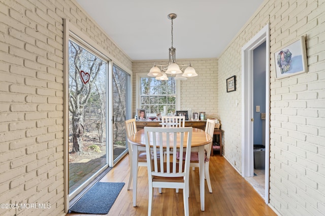 dining area featuring light wood-style flooring, brick wall, and an inviting chandelier