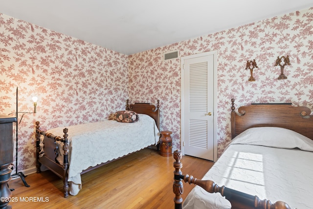 bedroom featuring wallpapered walls, visible vents, and wood finished floors