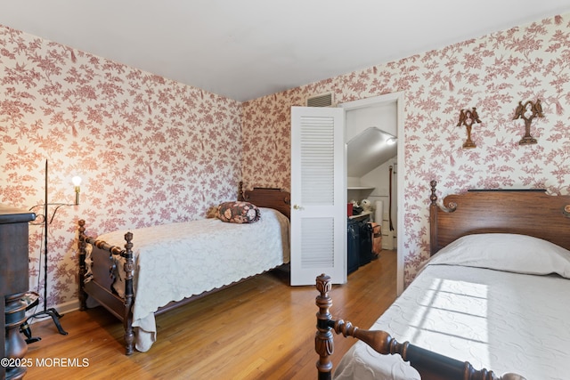 bedroom with wood finished floors, visible vents, and wallpapered walls