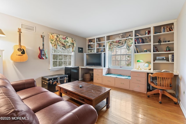 living area featuring visible vents, built in desk, and light wood finished floors