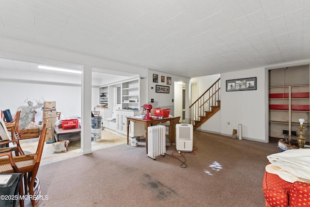 finished below grade area featuring carpet floors, visible vents, baseboards, stairs, and radiator heating unit